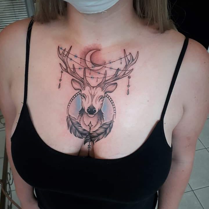 Татуировка оленя с полумесяцем и перьями на груди у девушки